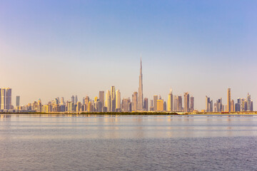 Fototapeta na wymiar Dubai Downtown skyline landscape with reflections in Dubai Creek, warm golden colors, seen from Dubai Creek Harbour promenade.