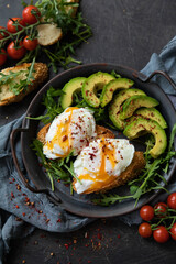Breakfast with poached egg, avocado and arugula. Served in a cast-iron pan on a textile background. Top view