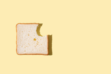 A slice of bitten bread on a yellow background in bright sunlight, a slice of bread for toast.