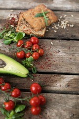 Copy space. On a wooden background, on the left, cherry tomatoes, avocado, garlic bun, herbs and sunflower seeds are laid out with vegetables. Rustic style of healthy eating. Vertical orientation