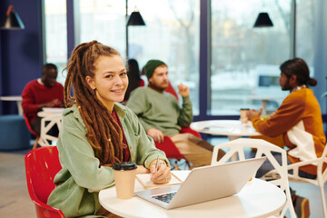 Happy young contemporary businesswoman with pencil making notes in notebook