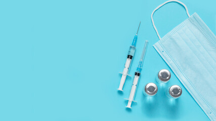 syringes, vials of vaccinations and a medical mask on a blue background. vaccination against...