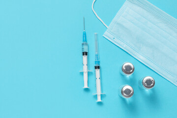 syringes, vials of vaccinations and a medical mask on a blue background. vaccination against...