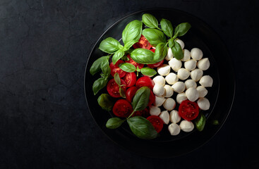 Mozzarella with tomato and basil on a black stone table.