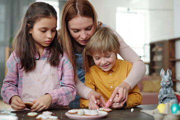 Obraz premium Young mother helping her little son and daughter with baking cookies for Easter