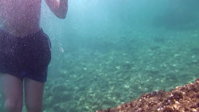 Turquoise water, sea bedrock, seaweeds, seabed, and some guys bathing.