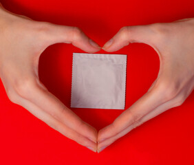 Condom ready to use in female  hands and heart shape hands sign on red background. Love and Safe sex concept.