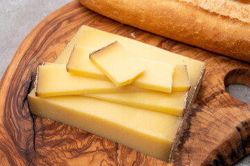 French food -  piece of cheese comte made from cow milk in region Franche-Comte in France and fresh baked baguette bread.
