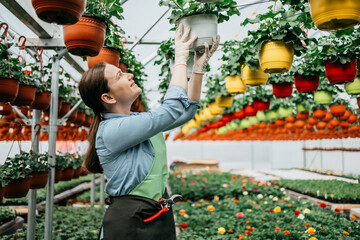 Fototapeta premium Happy and positive young adult woman working in greenhouse and enjoying in beautiful flowers.