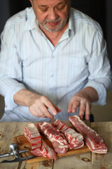A male chef cuts raw pork ribs. Preparing pork ribs for barbecuing or grilling. Cooking and cutting pork.