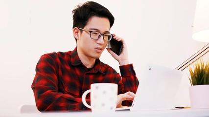 Young asian businessman working on desk at home and having phone conversation. High quality photo