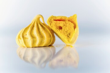 Yellow homemade meringues on a white reflective background, close up, isolated