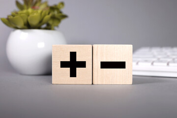 Opposites concept, wooden blog with plus and minus on GRAY background, flat lay, copy space, top view.