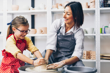 Happy mother and daughter making clay pottery on a spin wheel.