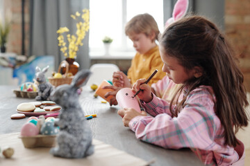 Cute little girl with highlighter drawing face of Easter rabbit on rolled paper