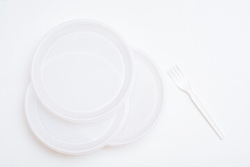 Three white disposable clean plastic plates and a fork on a white background. Top view