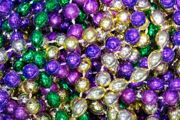 Mardi Gras beads of different colors scattered around, flat lay macro vibrant color splash background.
