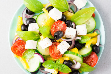 Fresh homemade greek salad with basil leaves on a plate on the table. Domestic life. Top view....