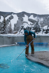 The pool guy cleaning the pool with the ski area in the background.