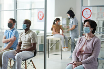 Mature woman and other patients in protective masks sitting on chairs in clinics