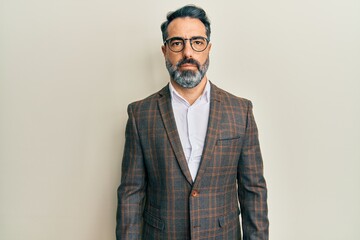 Middle age man with beard and grey hair wearing business jacket and glasses relaxed with serious expression on face. simple and natural looking at the camera.