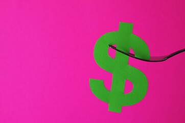 A green dollar sign is placed on a fork on a pink background with a copy space. Conceptual collage about currency in the style of minimalism. High quality photo