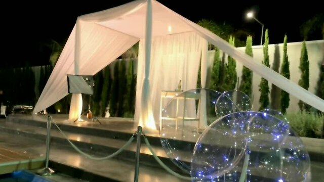 Jewish traditions wedding outdoor ceremony. Wedding canopy (chuppah, hupa) made of white fabric against the background of evening sky, palms and an artificial reservoir decorated with balloons. HD