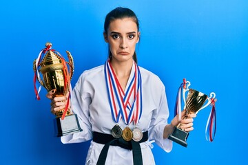 Beautiful brunette young woman wearing karate fighter uniform and medals holding trophy depressed and worry for distress, crying angry and afraid. sad expression. © Krakenimages.com