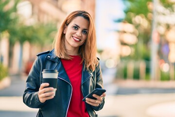 Young latin woman using smartphone and drinking take away coffee at the city.