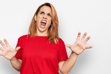 Hispanic young woman wearing casual red t shirt crazy and mad shouting and yelling with aggressive...