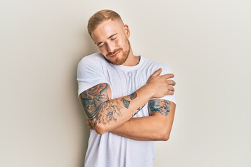 Young caucasian man wearing casual white tshirt hugging oneself happy and positive, smiling confident. self love and self care