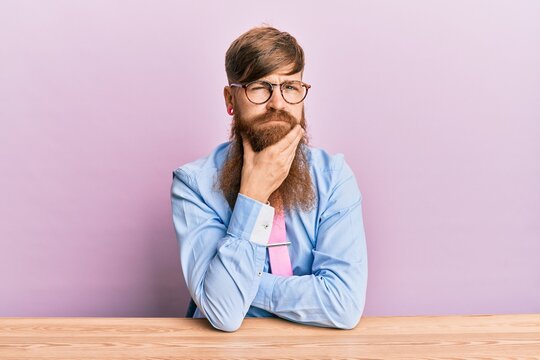 Young irish redhead man wearing business shirt and tie sitting on the table thinking looking tired and bored with depression problems with crossed arms.