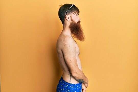 Redhead man with long beard wearing swimsuit and sunglasses looking to side, relax profile pose with natural face with confident smile.