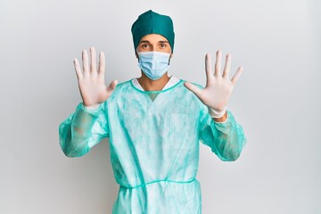 Young handsome man wearing surgeon uniform and medical mask showing and pointing up with fingers number ten while smiling confident and happy.
