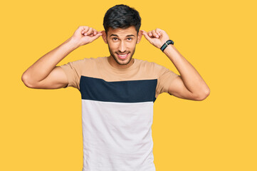 Young handsome man wearing casual clothes smiling pulling ears with fingers, funny gesture....