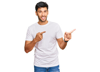 Young handsome man wearing casual white tshirt smiling and looking at the camera pointing with two hands and fingers to the side.