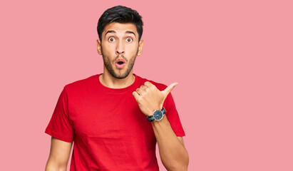 Young handsome man wearing casual red tshirt surprised pointing with hand finger to the side, open mouth amazed expression.