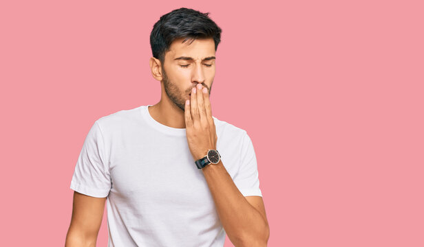 Young handsome man wearing casual white tshirt bored yawning tired covering mouth with hand. restless and sleepiness.