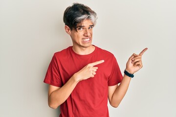 Young hispanic man wearing casual clothes pointing aside worried and nervous with both hands,...