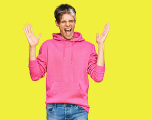 Fototapeta premium Young hispanic man wearing casual pink sweatshirt celebrating mad and crazy for success with arms raised and closed eyes screaming excited. winner concept