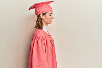 Young caucasian woman wearing graduation cap and ceremony robe looking to side, relax profile pose...