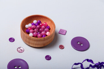 Close up of box of beads and buttons, tape or ribbon for sewing and embroidery. Purple set of materials for handcraft, making of bijouterie and accessories. White background, copy space.