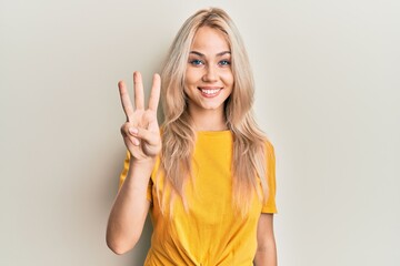 Beautiful caucasian blonde girl wearing casual tshirt showing and pointing up with fingers number three while smiling confident and happy. - obrazy, fototapety, plakaty