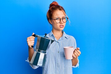 Young redhead woman drinking italian coffee clueless and confused expression. doubt concept.