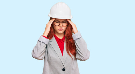 Young redhead woman wearing architect hardhat with hand on head for pain in head because stress. suffering migraine.