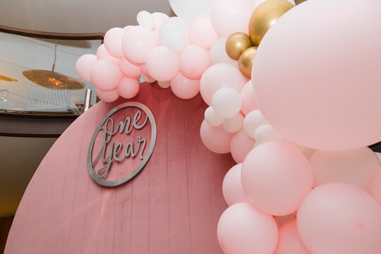Beautiful festive decorations, pink and white balloons arch and number one on wooden round background. Little 1 year old girl birthday party photo zone.