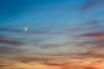 Fototapeta na wymiar Golden hour orange sky with small moon behind the clouds