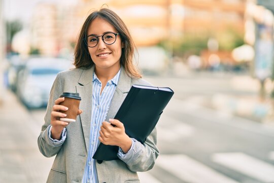 Young hispanic businesswoman using smartphone and drinking take away coffee at the city.