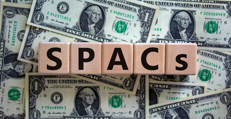 SPACs symbol. Wooden cubes with words 'SPACs, special purpose acquisition companies' on beautiful background from dollar bills, copy space. Business and SPACs concept.