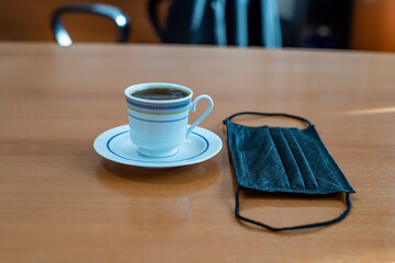 Coffee and mask in cafe on wooden table. New normal concept